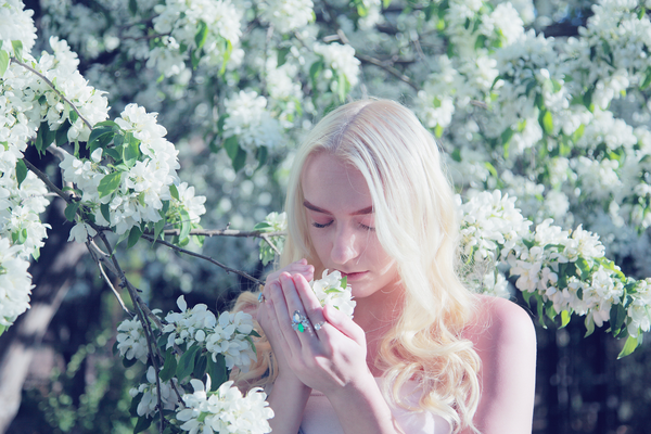 young blonde woman smelling spring flowers in blossom